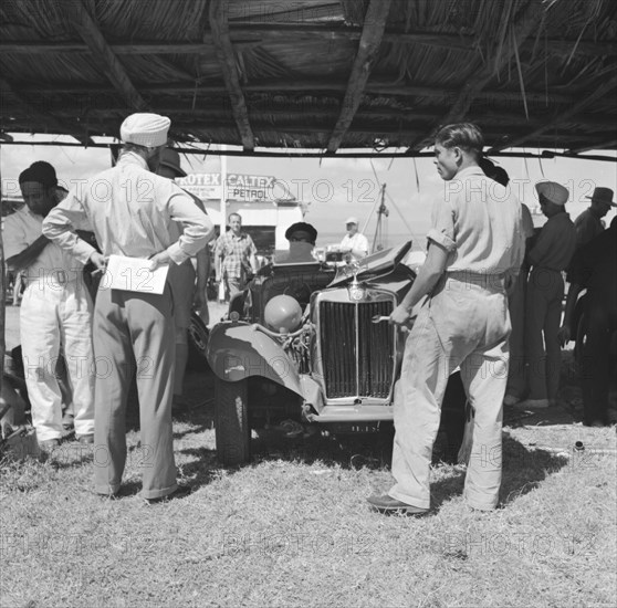 MG at the Langa Langa Races. An Asian man ponders the open engine of an MG car in the paddock at Langa Langa motor racing circuit. Langa Langa, Kenya, 13 October 1952. Langa Langa, Rift Valley, Kenya, Eastern Africa, Africa.