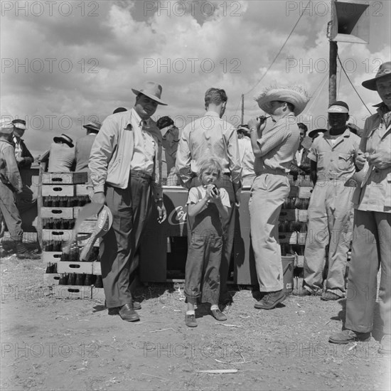 Coca Cola at Langa Langa. A child enjoys a bottle of Coca Cola from a drinks stand busy with customers at the Langa Langa racing circuit. Langa Langa, Kenya, 13 October 1952. Langa Langa, Rift Valley, Kenya, Eastern Africa, Africa.