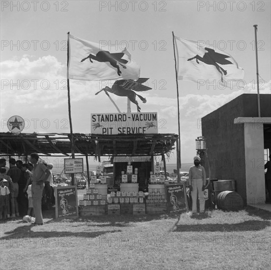 Standard-Vacuum Pit Service'. A turbaned Indian man stands beside a stall selling Mobil oil at the Langa Langa racing circuit, identified by a sign on its roof that reads: ' Standard-Vacuum Pit Service'. Langa Langa, Kenya, 13 October 1952. Langa Langa, Rift Valley, Kenya, Eastern Africa, Africa.