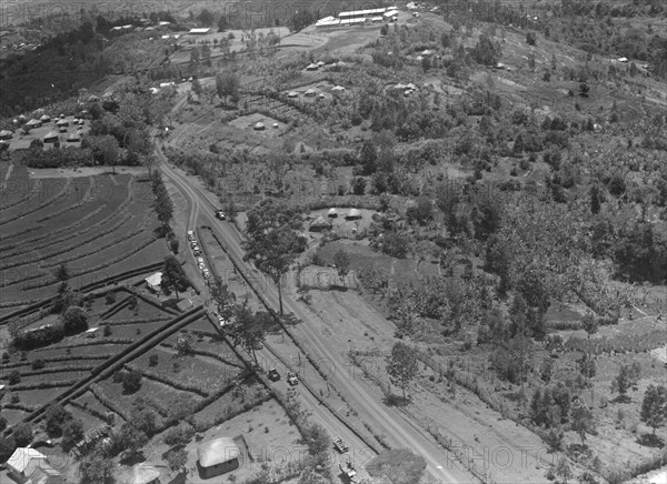 Air patrol over Littleton's town'. Aerial view taken from a patrol plane of a city identified by the photographer as 'Littleton's town'. This shot focuses on a large road running through an agricultural area of terraced farmland. Kenya, 1 November 1952. Kenya, Eastern Africa, Africa.