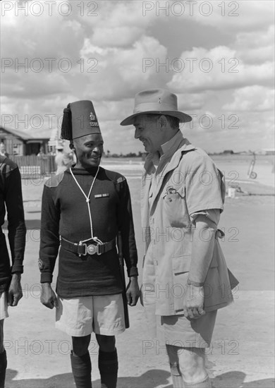 Clarke Gable jokes with an askari. Hollywood film star Clarke Gable jokes with a uniformed askari (soldier) on his arrival at Eastleigh airport. Gable is dressed in safari gear and was due to play the lead role in 'Mogambo', a John Ford film being shot on location in Kenya. Nairobi, Kenya, 7 November 1952. Nairobi, Nairobi Area, Kenya, Eastern Africa, Africa.