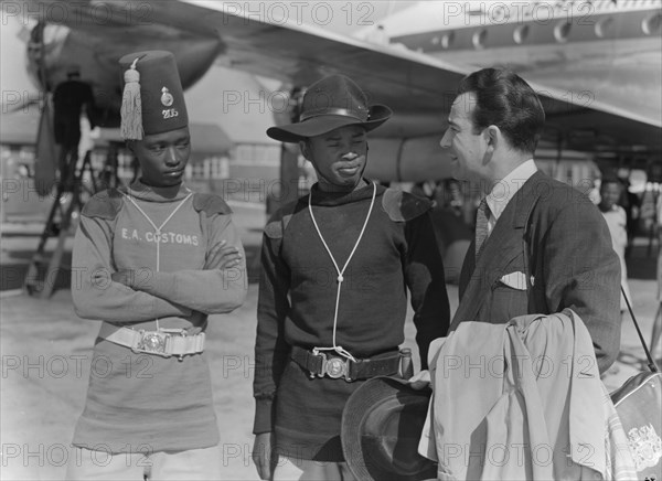 John Bentley with customs officials. Hollywood film star John Bentley chats to two uniformed customs officials after landing at Eastleigh airport. Nairobi, Kenya, 9 November 1952. Nairobi, Nairobi Area, Kenya, Eastern Africa, Africa.