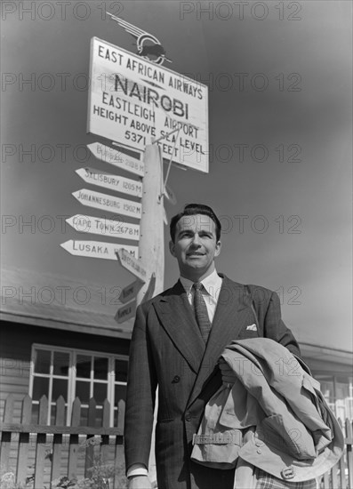 John Bentley at Nairobi airport. Hollywood film star John Bentley poses in front of a signpost after arriving at Eastleigh airport. Nairobi, Kenya, 9 November 1952. Nairobi, Nairobi Area, Kenya, Eastern Africa, Africa.