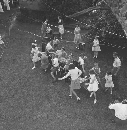 Musical chairs. Overhead view of children at the Button's party playing musical chairs in a garden. Kenya, 14 December 1952. Kenya, Eastern Africa, Africa.