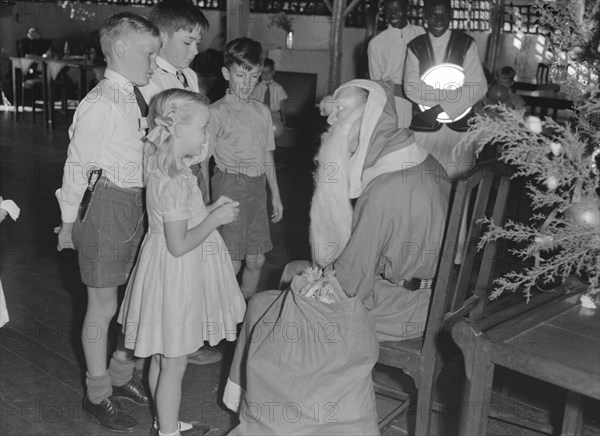 Father Christmas distributes gifts. Father Christmas distributes gifts to children at a Christmas party at the Forest Inn. Possibly Nairobi, Kenya, 25 December 1952. Kenya, Eastern Africa, Africa.