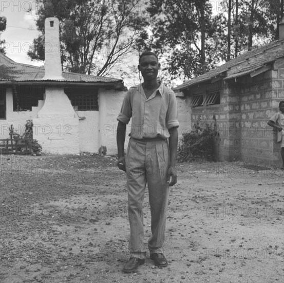 Off-duty Kenyan bartender. An off-duty Kenyan bartender relaxes with a cigarette, dressed in casual clothes outside a colonial building. Kenya, 1 January 1953. Kenya, Eastern Africa, Africa.