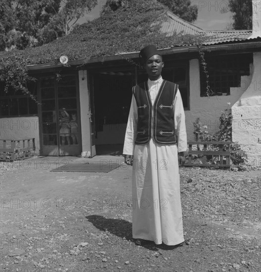 Uniformed Kenyan bartender. A uniformed Kenyan bartender poses for the camera outside a colonial building. Kenya, 1 January 1953. Kenya, Eastern Africa, Africa.