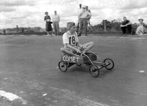 Number 18 in the soap box derby. An uneasy-looking boy rides to the finish line in his homemade go-cart 'Comet', entry number 18 in a soap box derby race. Kenya, 3 January 1953. Kenya, Eastern Africa, Africa.