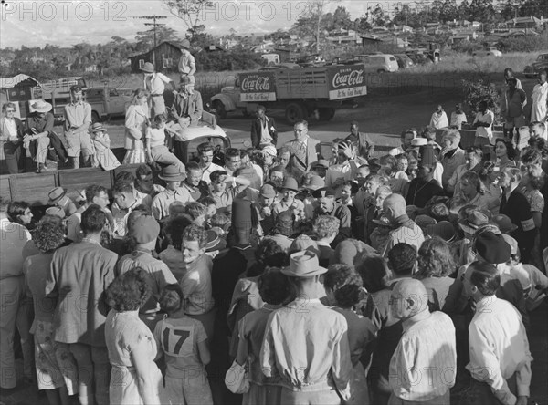 Soap box derby prize-giving. Onlookers crowd eagerly around child participants at the prize-giving speech of a soap box derby race. Kenya, 3 January 1953. Kenya, Eastern Africa, Africa.