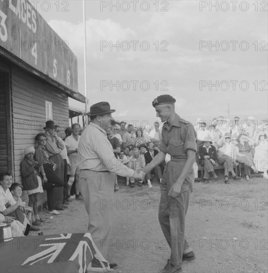 Handshake at the Nakuru Races. A young man wearing military uniform and beret shakes hands as he receives an award at a Nakuru Races prizegiving ceremony. Nakuru, Kenya, 15 September 1957. Nakuru, Rift Valley, Kenya, Eastern Africa, Africa.