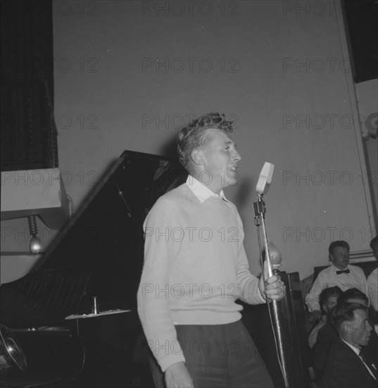 Jazz Ball singer. A casually dressed singer, supported by a band, clutches an upright microphone as he performs at a Jazz Ball. Kenya, 21 September 1957. Kenya, Eastern Africa, Africa.