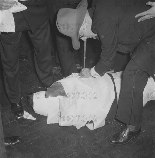 Rugby team antics. Members of a rugby team dressed in tuxedos fool around at the Mogambo Club. One of the men lies on the floor, having been 'mummified' in toilet paper by his friends. Possibly Nairobi, Kenya, 21 September 1957. Kenya, Eastern Africa, Africa.