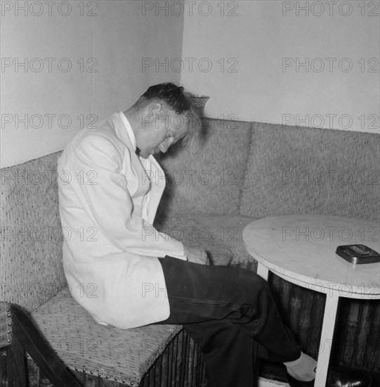 Worse for wear. A formally dressed man looks the worse for wear as he nods off in corner during a rugby team party at the Mogambo Club. Kenya, 21 September 1957. Kenya, Eastern Africa, Africa.