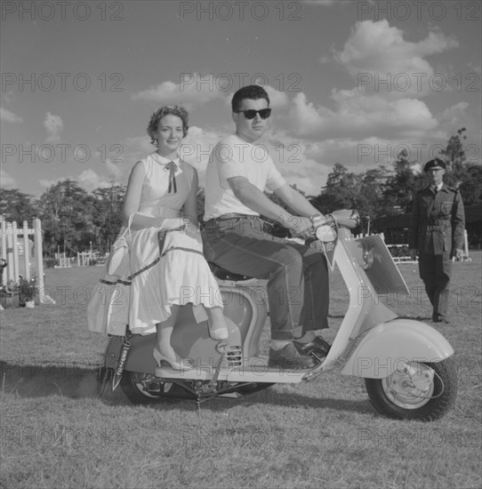 Couple on a scooter. A young couple in typical 1950s Western dress sit on a scooter in a vehicle parade at the Royal Show. Kenya, 25 September 1957. Kenya, Eastern Africa, Africa.