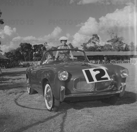 Number 12 on parade. A couple sit inside an open-top car marked with the number 12 at a vehicle parade at the Royal Show. Kenya 25 September 1957. Kenya, Eastern Africa, Africa.