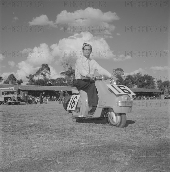 Scooter at the Royal Show. A European man sits on scooter number 16 in a vehicle parade at the Royal Show. Kenya, 25 September 1957. Kenya, Eastern Africa, Africa.
