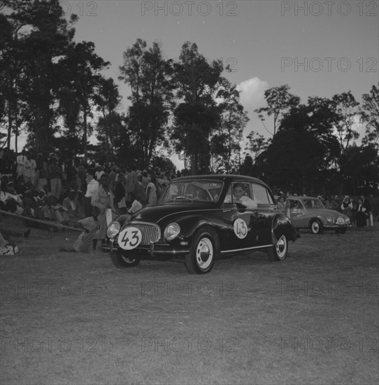 DKW in a vehicle parade. A man drives a DKW car past a crowd of onlookers during a vehicle parade at the Royal Show. Kenya, 25 September 1957. Kenya, Eastern Africa, Africa.