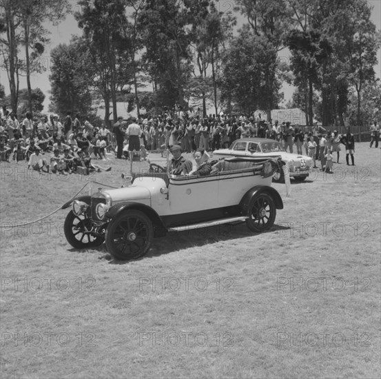 Austin convertible. A couple drive a Austin convertible car past onlookers in a vehicle parade at the Royal Show. Kenya, 28 September 1957. Kenya, Eastern Africa, Africa.