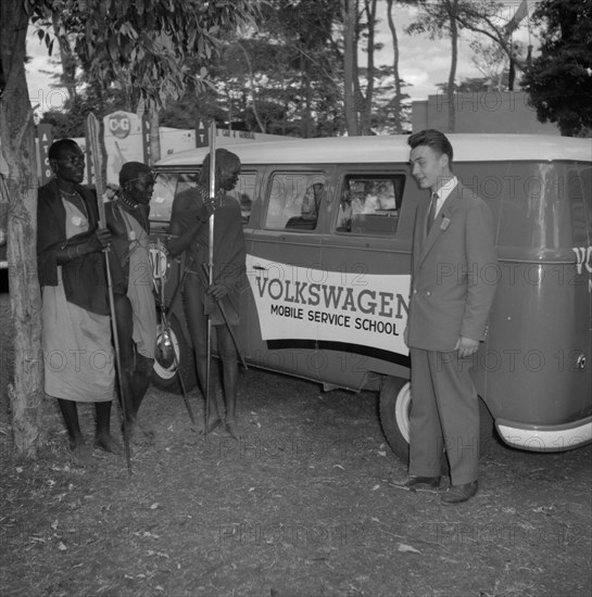 Volkswagen Mobile Service School. A European man introduces three Maasai warriors to a 'Volkswagen Mobile Service School' camper van, parked at the Cooper Motors stand at the Royal Show. Kenya, 25 September 1957. Kenya, Eastern Africa, Africa.