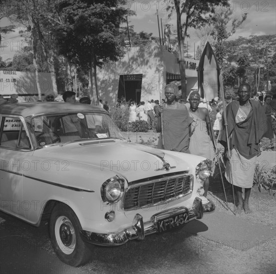 Maasai at Cooper Motors. Three Maasai warriors stand, holding spears, beside a shiny new car on display at the Cooper Motors stand at the Royal Show. Kenya, 25 September 1957. Kenya, Eastern Africa, Africa.