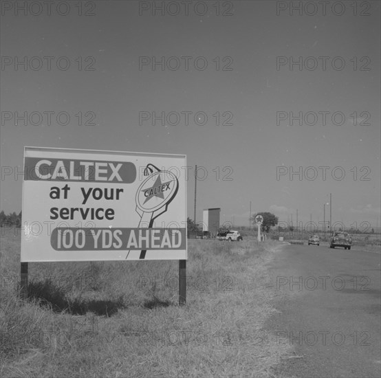 100 yards ahead'. A roadside sign indicates a Caltex Service Service approaching '100 yards ahead'. Kenya, 25 September 1957. Kenya, Eastern Africa, Africa.