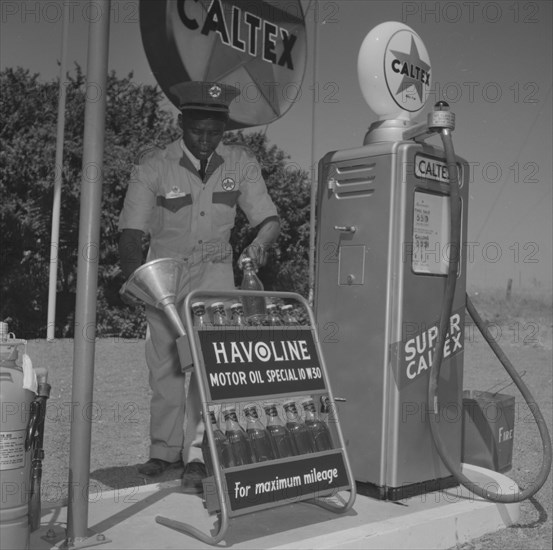 Havoline at Caltex. A uniformed attendant holds a funnel in one hand and a bottle of 'Havoline Motor Oil' in the other at a Caltex service station. Kenya,25 September 1957. Kenya, Eastern Africa, Africa.