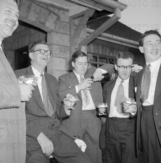 Champagne top-up. Five male wedding guests dressed in suits enjoy a champagne top-up at the Silver-McPherson wedding. Kenya, 5 October 1957. Kenya, Eastern Africa, Africa.