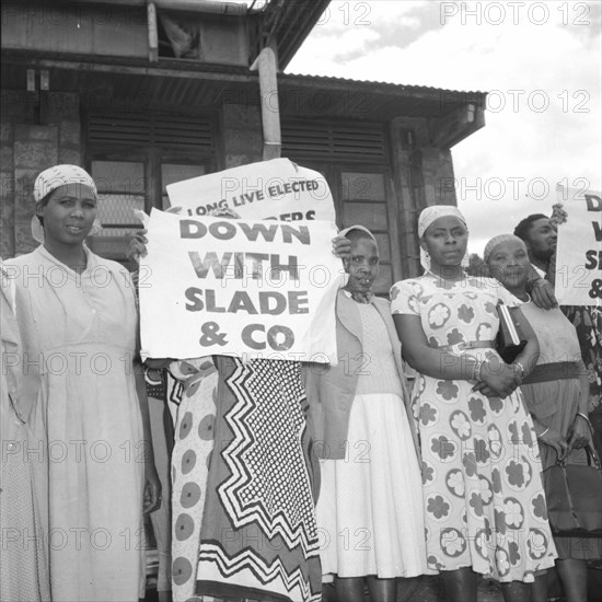 Female Kenyan demonstrators. Several Kenyan women involved in a peaceful demonstration at an airport, hold up placards on the arrival of politican Alan Tindal Lennox-Boyd. One of these reads: 'Down with Slade & Co'. Kenya, 11 October 1957. Kenya, Eastern Africa, Africa.