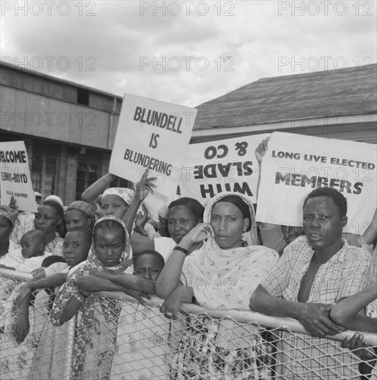 Kenyan demonstrators. A peaceful crowd of Kenyan demonstrators are held back behind an airport barrier on the arrival of politican Alan Tindal Lennox-Boyd. Amongst the placards on display are two that read: 'Blundell is Blundering' and 'Long Live Elected Members'. Kenya, 11 October 1957. Kenya, Eastern Africa, Africa.