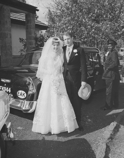 Hodgeson-Wilkinson wedding. Outdoors portrait of the newlywed Hodgson-Wilkinson couple, smiling for the camera before they depart in a waiting car. Kenya, 12 October 1957. Kenya, Eastern Africa, Africa.