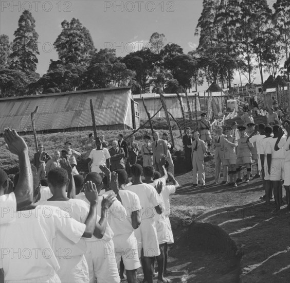 Lennox-Boyd meets Kenyan detainees. Alan Tindal Lennox-Boyd (1904-1983) meets Kenyan detainees being held at a fenced military camp. The detainees, seen from behind, are uniformly dressed in white and hold their hands up to order. Kangema, Kenya, 15 October 1957. Kangema, Central (Kenya), Kenya, Eastern Africa, Africa.