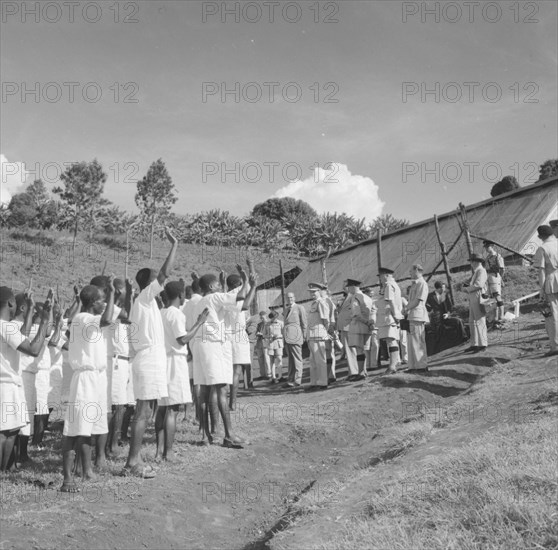 Lennox-Boyd meets Kenyan detainees. Alan Tindal Lennox-Boyd (1904-1983) meets Kenyan detainees being held at a fenced military camp. The detainees, seen in profile, are uniformly dressed in white and hold their hands up to order. Kangema, Kenya, 15 October 1957. Kangema, Central (Kenya), Kenya, Eastern Africa, Africa.