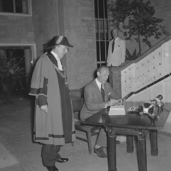Lennox-Boyd opens City Hall. Alan Tindal Lennox-Boyd (1904-1983) signs the visitors book at the opening of City Hall. A mayor dressed in his robes and chain witnesses the proceedings. Nairobi, Kenya, 16 October 1957. Nairobi, Nairobi Area, Kenya, Eastern Africa, Africa.