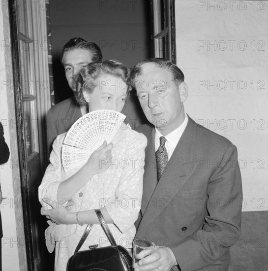 Prudential Insurance cocktail party. A woman whispers discreetly to her partner at a Prudential Insurance cocktail party, her mouth hidden behind her open fan. Kenya, 16 October 1957. Kenya, Eastern Africa, Africa.