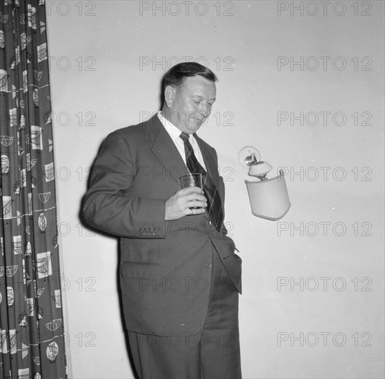 Prudential Insurance cocktail party. A suited businessman leans against the wall, glass in hand, at a Prudential Insurance cocktail party. Kenya, 16 October 1957. Kenya, Eastern Africa, Africa.