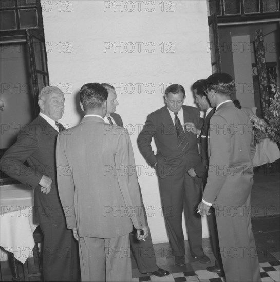 After dinner conversation. A group of suited businessmen huddle together, deep in discussion, at a Prudential Insurance cocktail party. Kenya, 16 October 1957. Kenya, Eastern Africa, Africa.