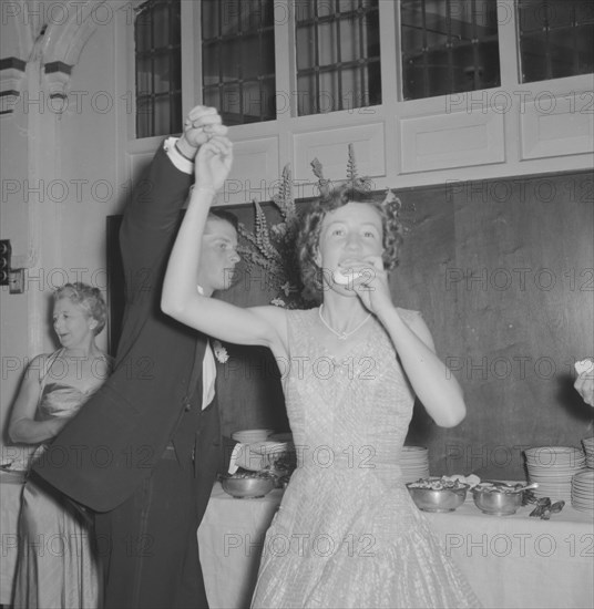 Dancing at the Limuru Hunt Ball. A young woman dressed in evening wear eats with one hand as she is spun round by her dance partner at the Limuru Hunt Ball. Kenya, 19 October 1957. Kenya, Eastern Africa, Africa.