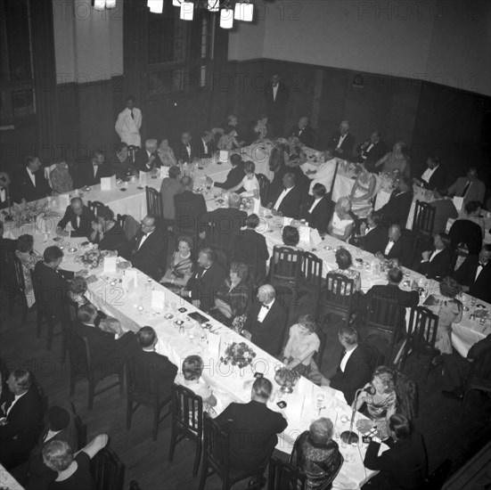 KNFU dinner. Overhead view of a Kenyan National Farmer's Union (KNFU) dinner. Formally dressed male and female guests sit around long banquet tables laid with floral displays and menus. Kenya, 5 November 1957. Kenya, Eastern Africa, Africa.