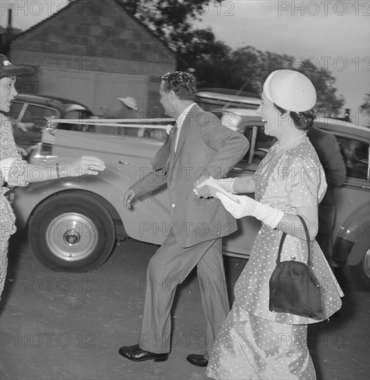 Newlyweds make a dash. The newlywed Coltart couple make a dash for their wedding car under a shower of confetti thrown by guests. The bride wears a polka dot skirt suit and clutches her handbag as she runs. Kenya, 9 November 1957. Kenya, Eastern Africa, Africa.