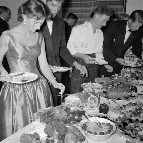 Buffet supper. Formally dressed guests at the Orme-Smith 21st birthday party queue up to help themselves to a luxurious buffet supper. Kenya, 9 November 1957. Kenya, Eastern Africa, Africa.