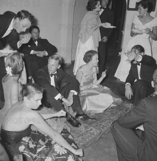 Animated socialising. A group of animated young men and women dressed in formal attire socialise at the Orme-Smith 21st birthday party. Kenya, 9 November 1957. Kenya, Eastern Africa, Africa.