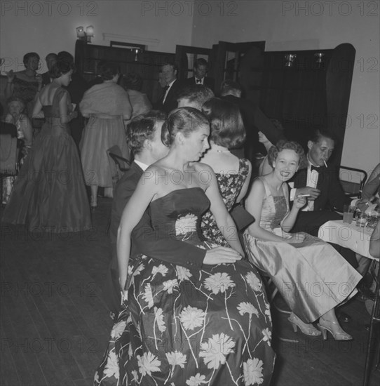 Comfortable chair. A young woman in a sleeveless floral party dress sits on a man's knee at the Orme-Smith 21st birthday party. Kenya, 9 November 1957. Kenya, Eastern Africa, Africa.