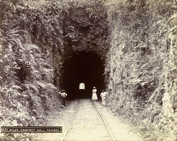 Extension from Porus to Montego Bay. A woman and two men stand at the entrance to a railway tunnel cut through a rockface. The original caption identifies this as 'Comfort Hall Tunnel', located on an extension line running between Porus and Montego Bay. Jamaica, circa 1895. Jamaica, Caribbean, North America .