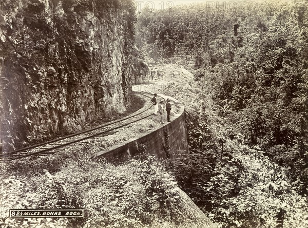 Railway track at Bonas Rock. Three men stand on a stretch of railway track that clings to the side of an overgrown mountain at Bonas Rock. Jamaica, circa 1895. Jamaica, Caribbean, North America .