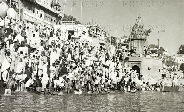 Religious pilgrims at Benares. Religious pilgrims crowd the steps of a bathing ghat (stepped wharf) on the River Ganges at Benares, one of Hinduism's holiest sites. The famous Hindu temples of Scindia Ghat and Manikarnika Ghat are located nearby. Benares, United Provinces (Varanasi, Uttar Pradesh), India, circa 1925. Varanasi, Uttar Pradesh, India, Southern Asia, Asia.