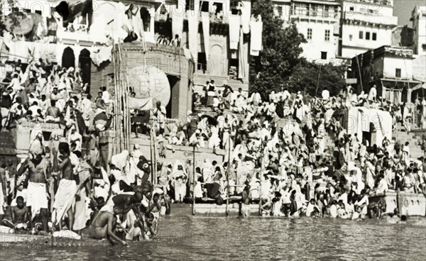 Religious pilgrims at Benares. Religious pilgrims crowd the steps of a bathing ghat (stepped wharf) on the River Ganges at Benares, one of Hinduism's holiest sites. The famous Hindu temples of Scindia Ghat and Manikarnika Ghat are located nearby. Benares, United Provinces (Varanasi, Uttar Pradesh), India, circa 1925. Varanasi, Uttar Pradesh, India, Southern Asia, Asia.