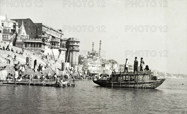 A bathing ghat at Benares. A boat on the River Ganges floats beside a religious bathing ghat (stepped wharf) at Benares, one of Hinduism's holiest sites. Hindu pilgrims visiting the nearby temples of Scindia Ghat and Manikarnika Ghat, can be seen descending the steps to bathe. Benares, United Provinces (Varanasi, Uttar Pradesh), India, circa 1925. Varanasi, Uttar Pradesh, India, Southern Asia, Asia.