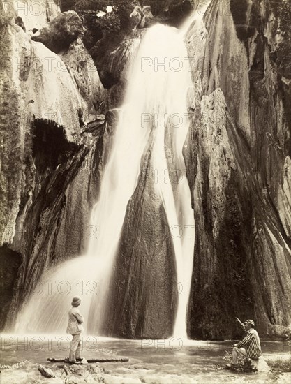 Waterfall, India. Two men in European dress view a waterall from the rocks at its base. India, circa 1885. India, Southern Asia, Asia.