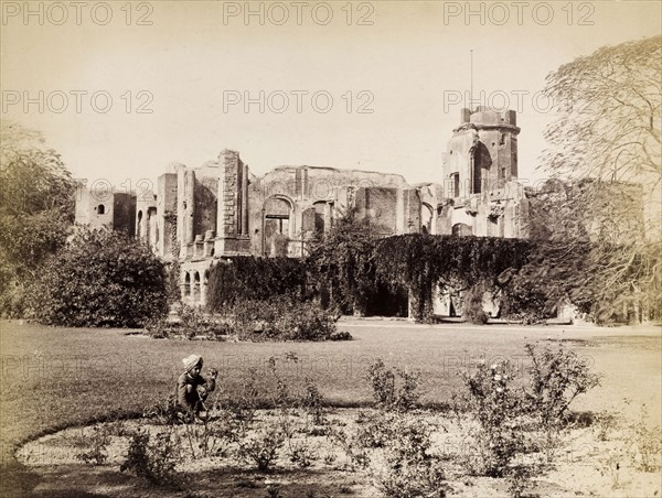 Ruins of the British Residency. The British Residency at Lucknow, ruined during the Indian Mutiny of 1857-8. The ruins are partially overgrown with climbing plants and an empty flagstaff protrudes from a tower. In the foreground, an Indian boy squats, tending to a small circular bed of roses. Lucknow, North Western Provinces (Uttar Pradesh), India, circa 1885. Lucknow, Uttar Pradesh, India, Southern Asia, Asia.
