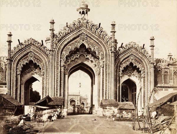 Gateway to the Hussainabad Imambara. The decorative arches of the gateway leading to the Hussainabad Imambara. Makeshift shops and stalls line the road in front of the gate. Lucknow, North Western Provinces (Uttar Pradesh), India, circa 1875. Lucknow, Uttar Pradesh, India, Southern Asia, Asia.